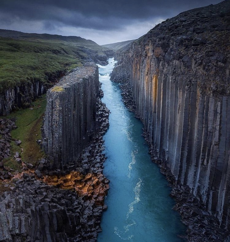 a scenic view of a river flowing through a canyon with basalt columns on either side under a cloudy sky.