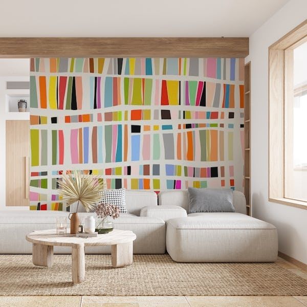 this is a minimalist living room with a white couch and a coffee table in front of a colorful abstract wall. the couch is a sectional with two pieces. the coffee table is made of wood and has a simple design. the rug is made of natural fibers and has a woven texture. the room is bright and airy and has a modern feel.