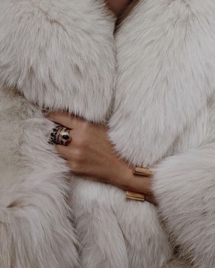 closeup view of a woman's hands adorned with gold rings and bracelets, partially visible as she holds the edges of a luxurious, long white fur coat. the fur is fluffy and soft, creating a texturerich image. the overall aesthetic is elegant, stylish, and luxurious, showcasing winter fashion and highend accessories.
