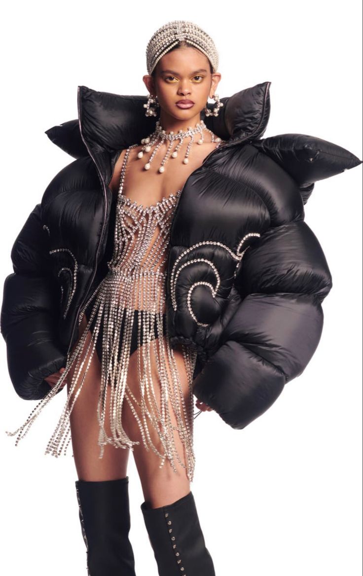 a fashion model wears a black puffer jacket with a diamondencrusted silver top and boots.  she has a silver headband and earrings on. the photo is likely taken in a studio and focuses on the model's clothing.