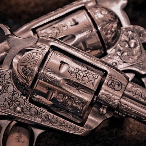 the image is a closeup shot of two intricately engraved revolvers, likely antique firearms. the revolvers are heavily ornamented with detailed floral and scrolllike designs etched into the metal. the color palette is muted browns and silvers, giving a vintage feel. the focus is sharp, highlighting the intricate metalwork and the serial number (51091896) visible on one of the guns.  the overall aesthetic suggests an old west or cowboy theme.