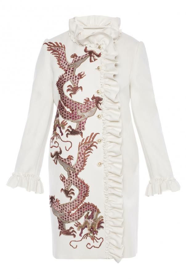 a white coat with a ruffled collar and ruffled trim down the front. an embroidered dragon design runs down the center of the coat.