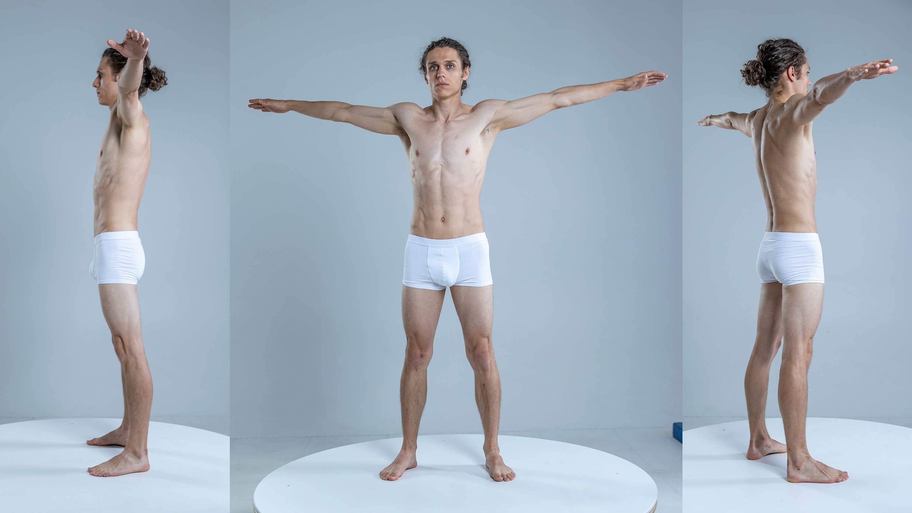 a muscular man in white underwear is posing in a studio. he is shown from three angles: side, front, and back. he has his arms extended out to his sides. the man is in good shape and has a strong physique. he is standing on a white platform. the background is a simple gray wall.