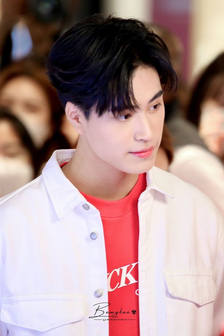 a closeup portrait of a young asian man with black hair and a friendly expression. he is wearing a white denim jacket over a red tshirt. the background is blurred, suggesting an indoor setting. the lighting is bright, illuminating the subject's face and creating a clear and engaging image.