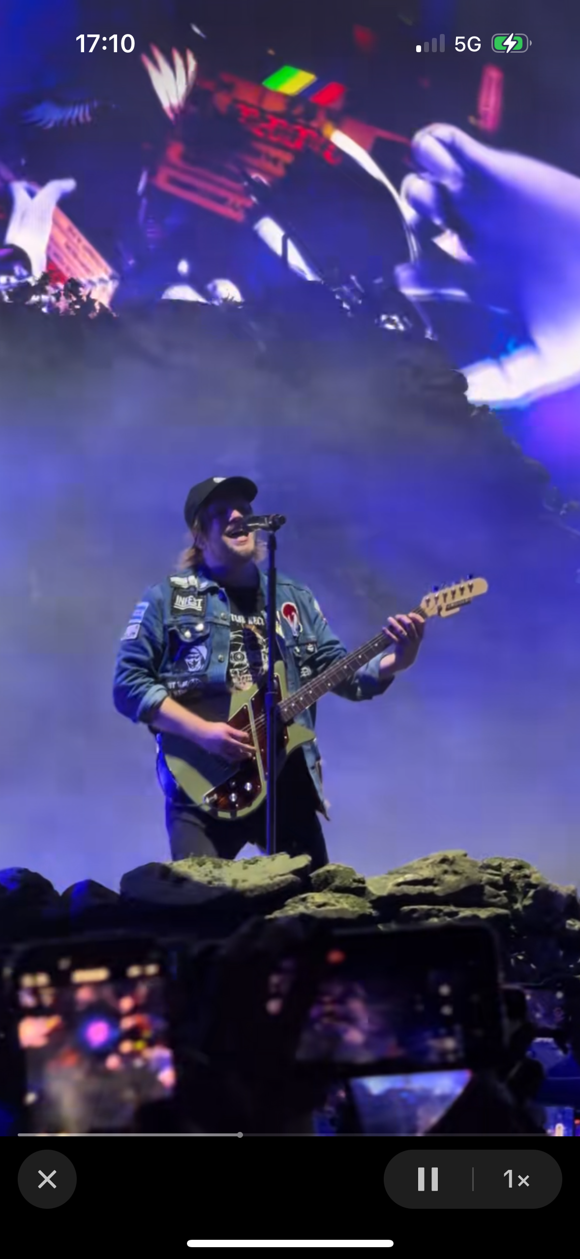 a man is singing and playing an electric guitar on a concert stage. he has a microphone in his hand and is surrounded by lights. the crowd can be seen in the background.  he is giving a passionate performance and the energy is high.