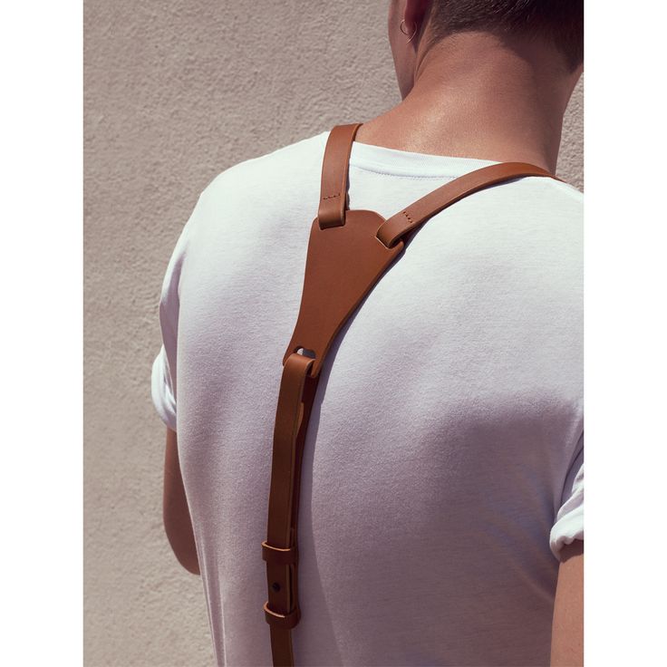 a man is wearing a brown leather strap on his back. the strap is connected to a white tshirt. the man is wearing a simple tshirt, and the strap is visible as a fashion accessory.