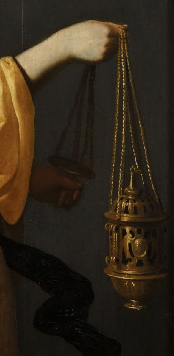 a hand is holding a chain attached to a golden incense burner, possibly a religious object. the hand is also holding a separate object with chains. the person is wearing yellow clothing. the background is dark.