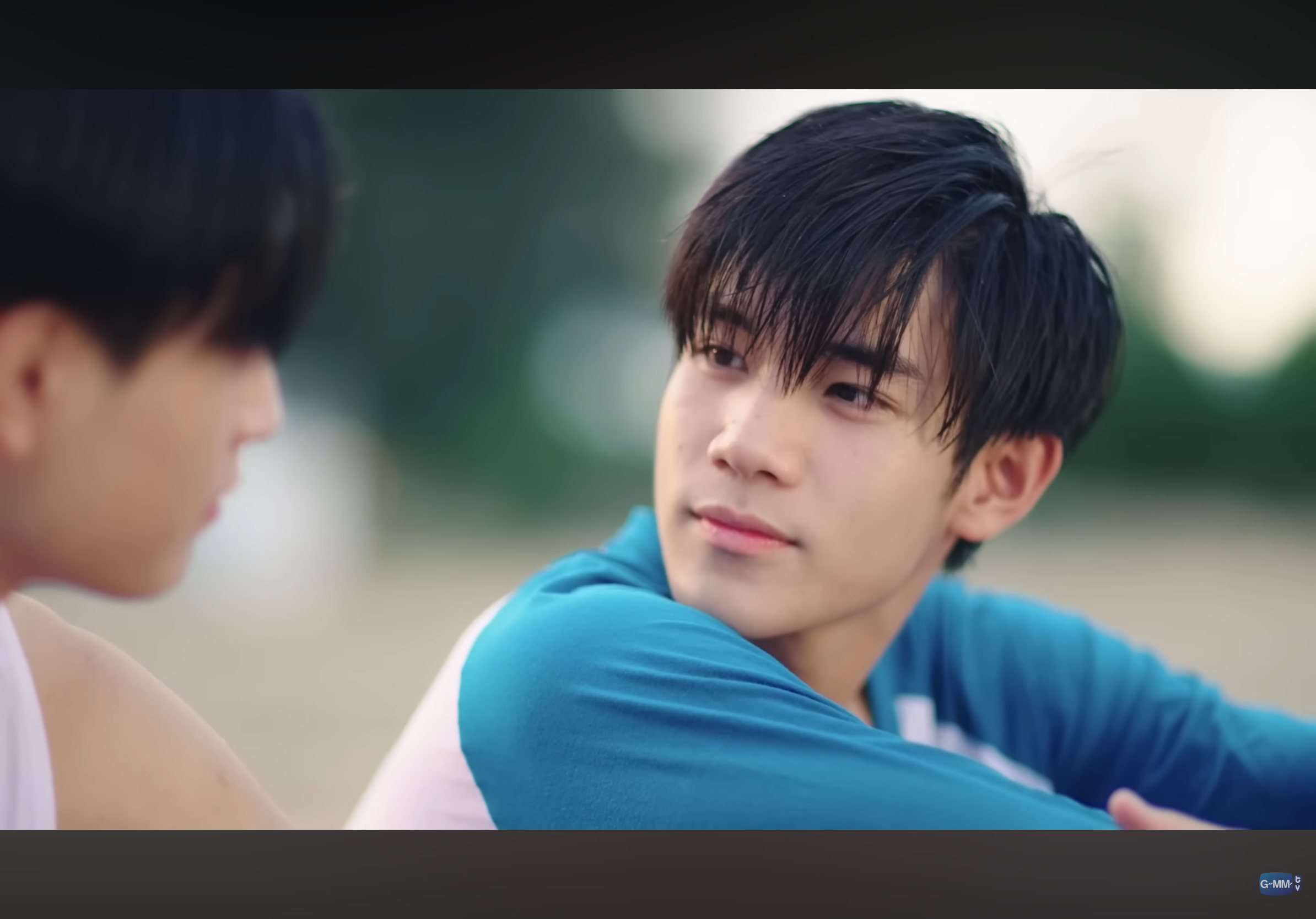 a closeup shot of two teenage boys in athletic wear on a beach at sunset. the boy on the right is looking back at the other boy with a slight smile. the warm lighting and the boys' proximity suggest a close relationship.