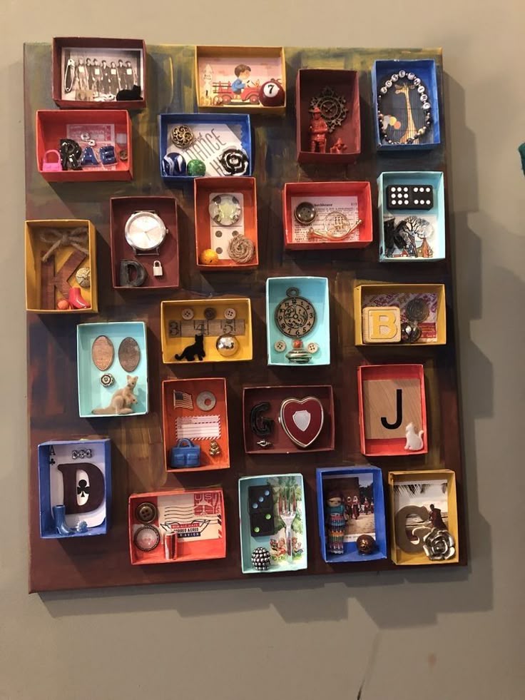 the image showcases a piece of wall art composed of numerous small, colorful shadow boxes. each box contains a unique collection of miniature items and trinkets, creating an eclectic and whimsical assemblage. the boxes are arranged in a grid pattern against a painted canvas background. the contents include items such as watches, buttons, small toys, vintage objects, letters of the alphabet, dice, pieces of jewelry, coins, and small figurines. the overall impression is of a handcrafted collage, filled with found objects and creating a decorative and personalized display.