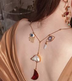 a woman wearing a gold necklace with eye, moon and shell pendants. the necklace hangs down her back and is intricate and ornate.