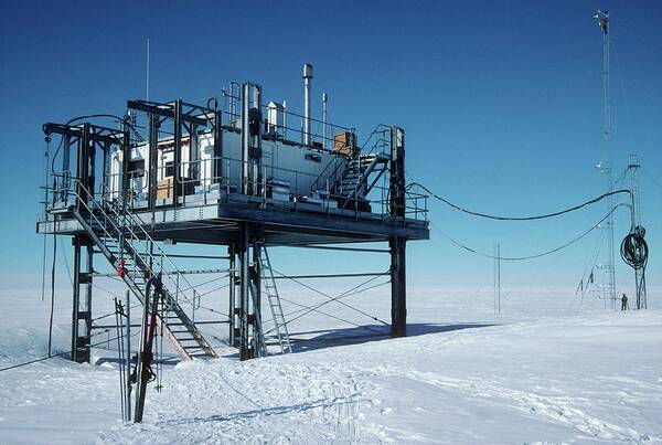 a research station in antarctica, with a platform supporting a building and equipment, surrounded by a vast expanse of snow and ice. in the distance, a tall antenna is visible, indicating a remote location. the station is likely involved in scientific research related to climate change, atmospheric monitoring, or other environmental studies.  the desolate landscape highlights the harsh conditions of antarctica, where scientists work to understand and address global issues.