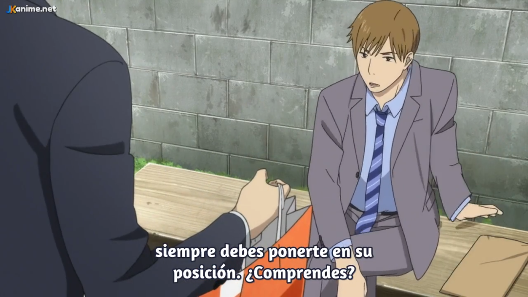 the image shows a scene from an anime, with two male characters sitting on a bench in what appears to be a park. one character, wearing a suit, is looking down and listening intently to the other character, who is partially offscreen. the visible character has a concerned expression.  the background features a plain concrete wall and suggests a daytime setting with slightly overcast lighting. the overall tone of the image is serious and contemplative.
