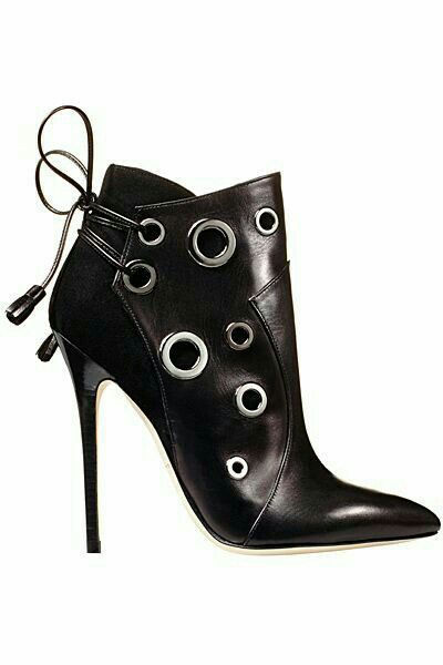 a black stiletto heel ankle boot with metal eyelets is shown in the image. the boot has a pointed toe and a high heel. the upper part of the boot is made of black leather and decorated with silver eyelets of different sizes. the back of the boot has a tie closure with thin strings.
