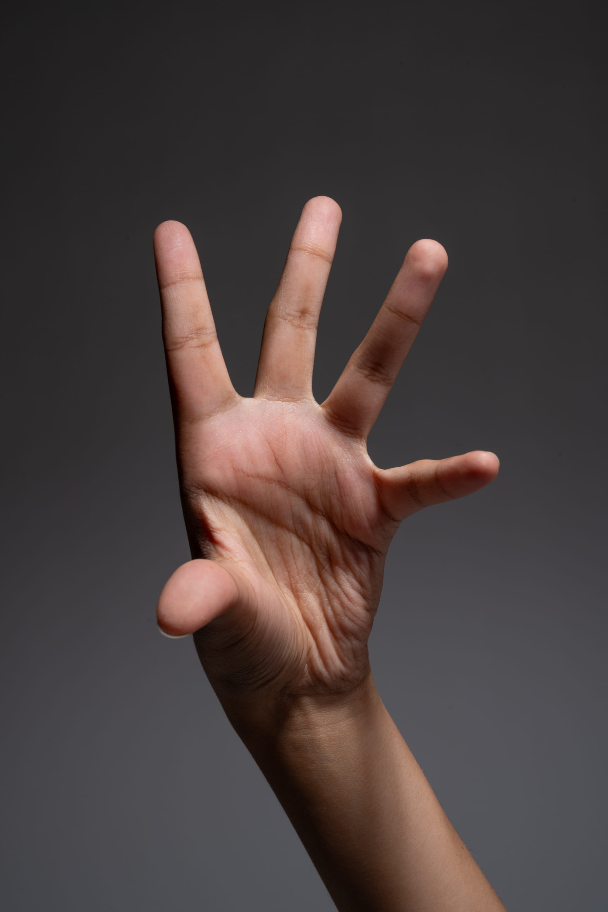 a closeup image of a hand with its fingers spread out against a dark gray background. the side lighting highlights the texture and details of the skin, creating a dramatic effect.