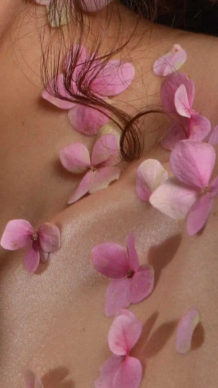 a closeup shot of a woman's shoulder and neck adorned with delicate pink flower petals. the petals are scattered across her skin, creating a soft and romantic atmosphere. the woman's hair is partially visible, and her skin appears smooth and healthy. the overall mood is serene and peaceful, suggesting a spa or relaxation setting. the image is softfocus and uses pastel tones, enhancing the gentle and feminine feel.