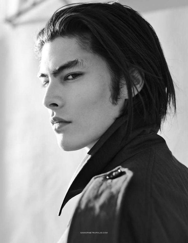 a black and white portrait of an asian male model looking over his shoulder. he has dark hair styled back from his face and is wearing a dark coat. he has a serious expression and prominent eyebrows.