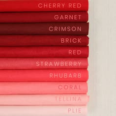 a vertical stack of fabric swatches in various shades of red, from deep cherry red at the top to pale pink at the bottom. each swatch has a white label with a color name printed on it. the labels are arranged in a gradient of color, going from dark to light. the image is a closeup view, and the background is white.
