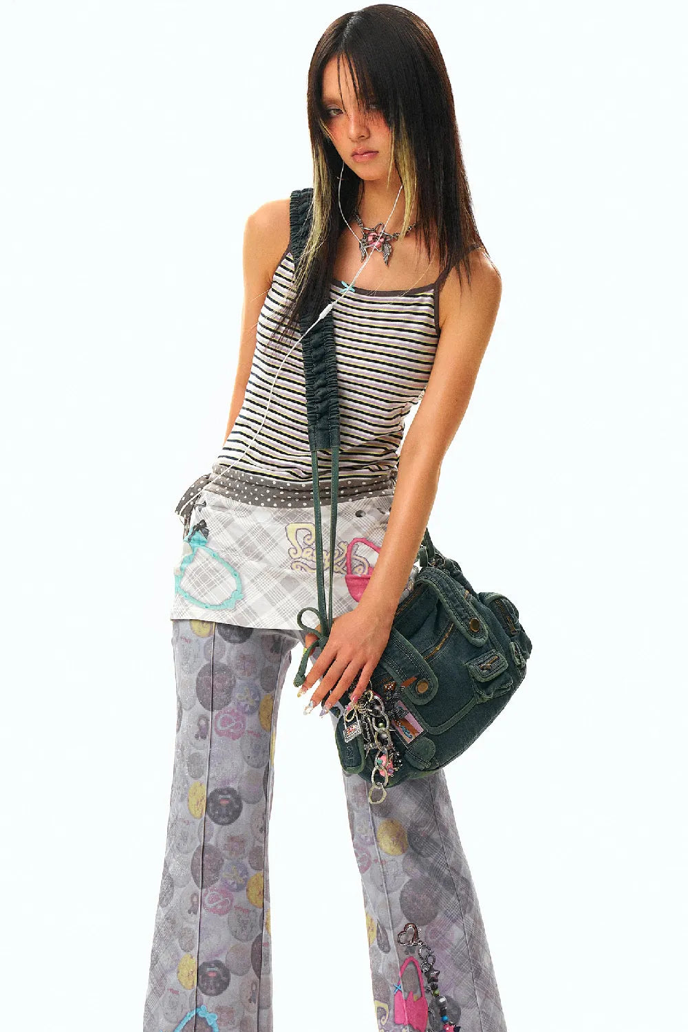 a full body shot of a young asian woman standing against a white background. she is wearing a striped tank top, a patterned skirt, and flared pants with a print. she has a dark shoulder bag and is wearing a necklace and earrings.  her hair is styled in a long, straight style with some lighter highlights. she is looking directly at the camera.
