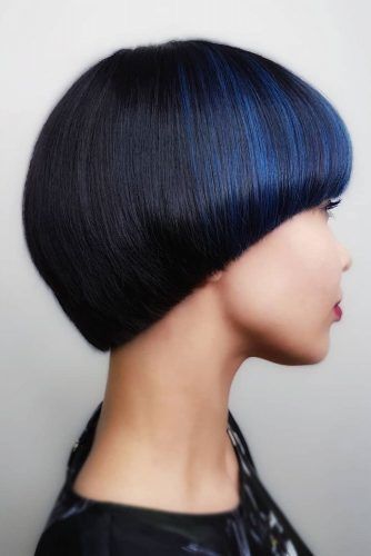a young asian woman with short, black hair, with a blue highlight on the top half, is looking to the right side of the frame. she's wearing a black outfit with a dark pattern. the image is a portrait and the background is white.
