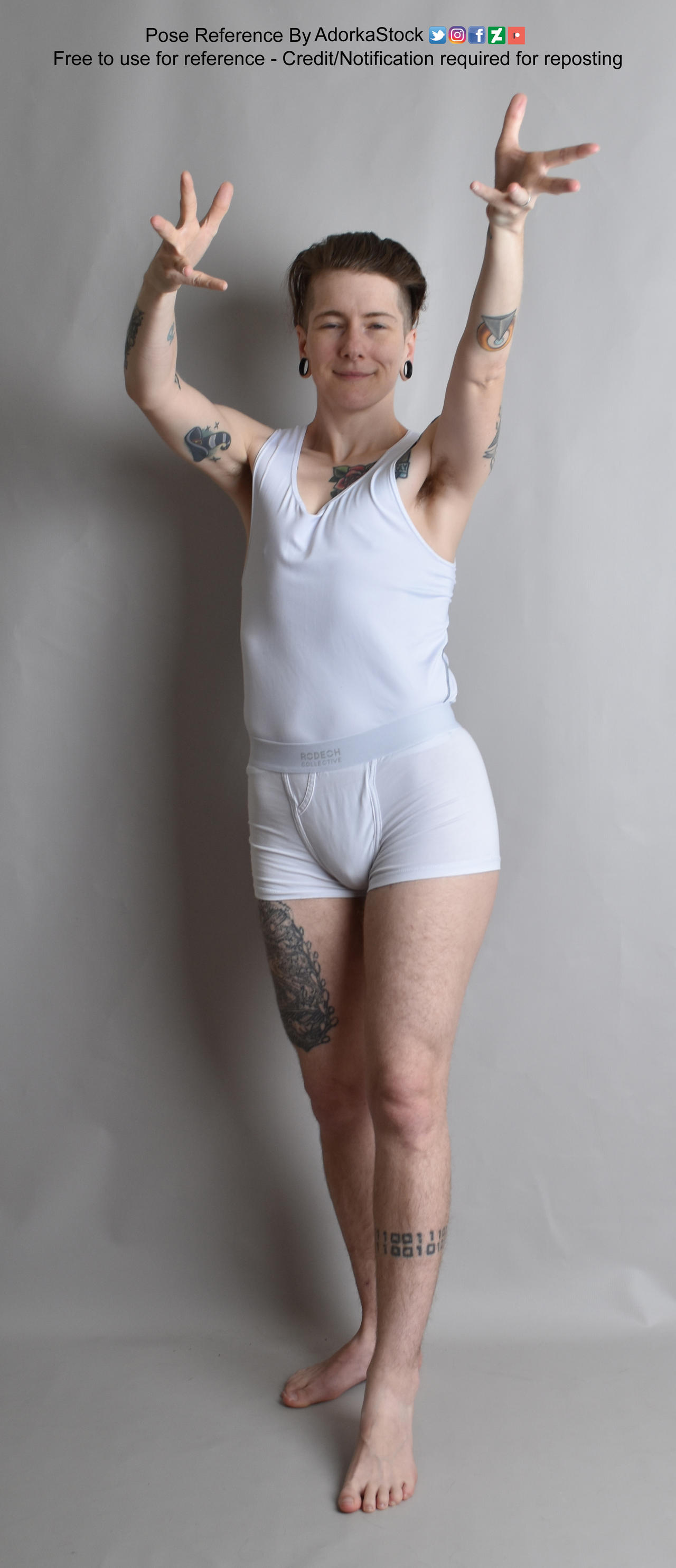 fullbody shot of a man standing with his arms raised above his head. he is wearing white underwear and a white tank top. he has tattoos on his arms and legs.  the background is a neutral grey.  the image is labeled as a "pose reference" indicating it's for artistic or design use.