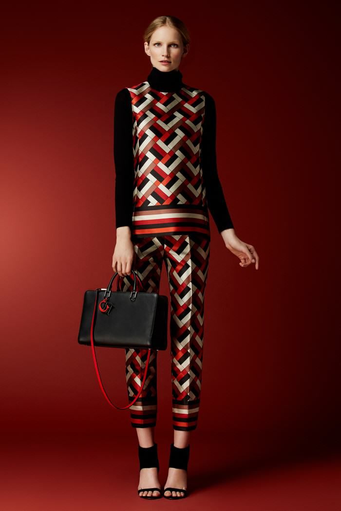 a fulllength studio shot of a fashion model wearing a stylish outfit. the outfit consists of a black turtleneck, a geometricpatterned sleeveless top and pants in shades of red, black, white and beige. the model is also carrying a black handbag with red accents and wearing black anklestrap heels. the background is a solid red color, enhancing the vibrancy of the outfit. the model's pose is elegant and poised. the overall image exudes sophistication and chic style.