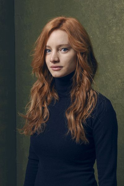a woman with long, flowing red hair is the subject of this portrait. she is wearing a simple black turtleneck, which accentuates her striking blue eyes and fair skin. the background is a mottled green, providing a subtle contrast to her fiery hair. the soft lighting enhances her features, creating a sense of warmth and intimacy.