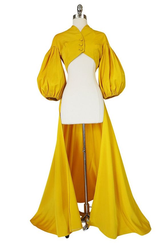 a canary yellow twopiece dress consisting of a cropped, highnecked jacket with dramatic puff sleeves and a floorlength, highwaisted skirt. the jacket features a buttonup front closure, and the ensemble is displayed on a headless mannequin against a white background.