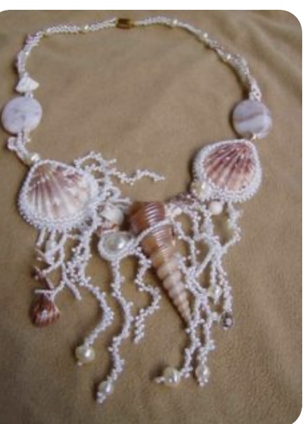 this is a closeup image of a seashell necklace on a beige background. the necklace features large cockle shells, a pointed shell as the centerpiece, white beads of varying sizes, and small brown shells. the shells are a mix of light brown and white, and the beads are a pearly white. the necklace has a delicate, feminine look and feel, and the natural elements give it a beachy, bohemian vibe.