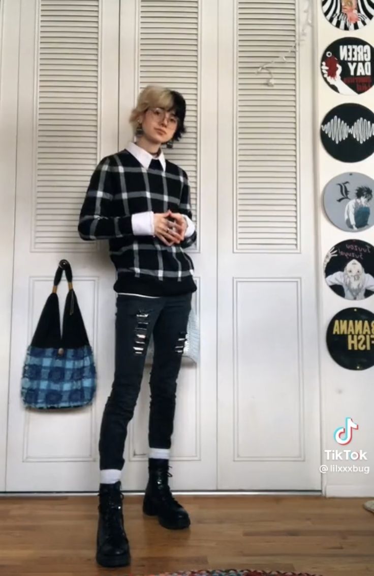 a fullbody shot of a person standing in front of a white closet door. they are wearing a black and white checkered sweater, black ripped jeans, combat boots, and white socks.  their hair is styled halfup, with one side blonde and the other side black. they are also wearing glasses and carrying a blue and black handbag. the wall behind them is decorated with various vinyl records.  a tiktok watermark is visible in the bottom right corner. the overall style is grungeinspired and alternative.
