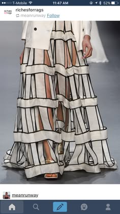 a woman wearing a white and black patterned skirt with a white jacket walks down a runway during a fashion show.