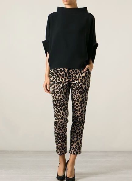 a woman wearing a black top and leopard print pants poses in a studio, against a white background. she is wearing high heels and has a chic and elegant style.
