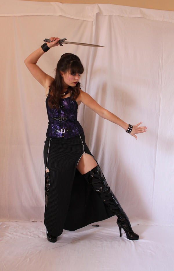 a fulllength shot of a young woman in a dark gothicstyle costume, holding a sword. she is wearing a purple corset, a black skirt with slits, and black thighhigh boots.  she's posing dramatically, as if in a fight or fantasy scene, against a plain white backdrop.