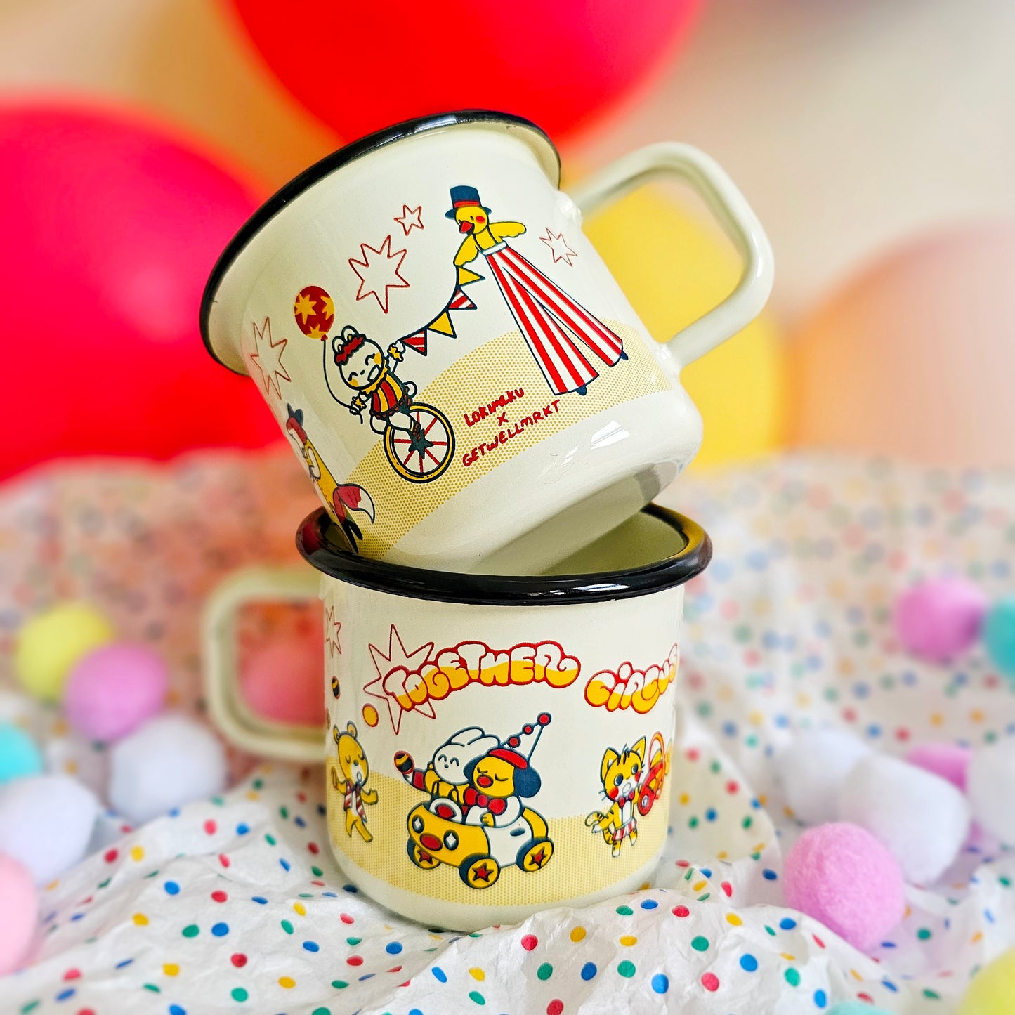 two adorable enamel mugs are stacked on top of each other.  the mugs feature a whimsical circus theme with cute cartoon characters and bright, pastel colors.  the design incorporates the names "lorinaku" and "getwellmarket", suggesting a collaboration. the mugs are sitting on a fabric surface with colorful pompoms scattered around, creating a festive and cheerful scene. the overall aesthetic is kawaii and playful.