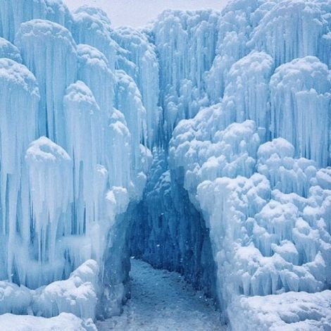 the image shows a frozen landscape with a large structure of ice and icicles forming a sort of ice cave or tunnel. the scene is dominated by blue and white tones, creating a wintery and frozen atmosphere. icicles hang from above, and snow covers the ground.
