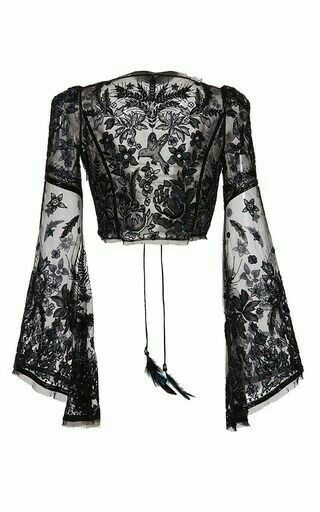 the image shows a black lace cropped blouse with long, bell sleeves and a floral pattern. it has a tie at the back with feathers attached. the view is from the back.