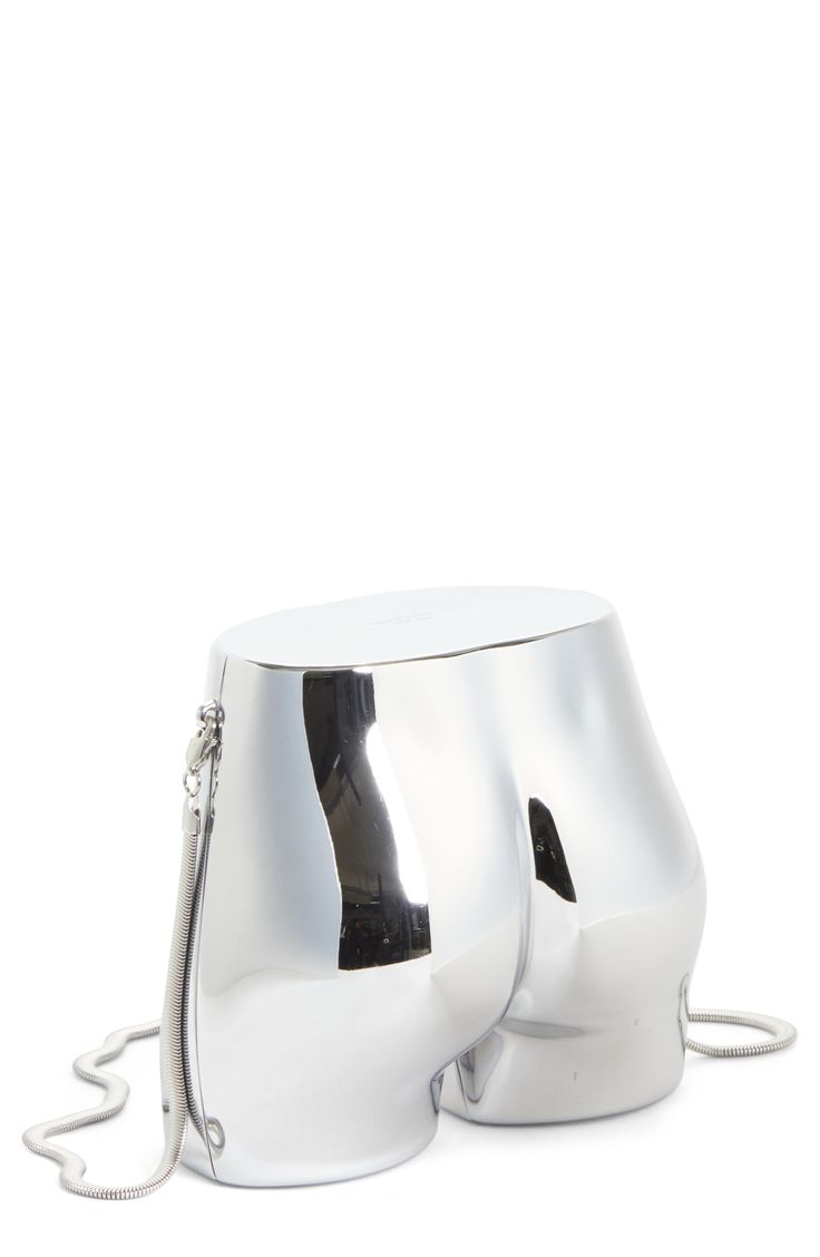 a closeup studio shot presents a highly reflective silver handbag shaped like a human buttocks. the bag features a zipper closure and a chain strap. the design is unusual and eyecatching, making it a statement fashion piece. the bright silver color and smooth, sculpted curves add to its modern and artistic aesthetic.