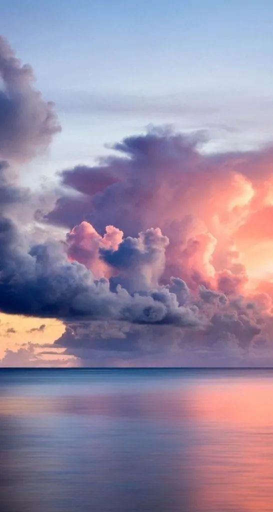 a serene and tranquil scene with a beautiful sky filled with pink, purple, and blue clouds reflecting on the calm ocean surface. the horizon line is barely visible as the sky blends seamlessly with the water. the soft light of the sunset or sunrise creates a dreamlike atmosphere.