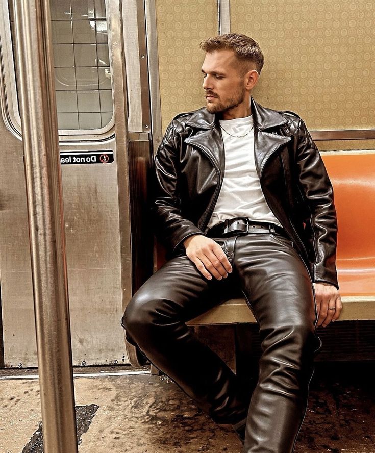 a stylish man in a black leather jacket and black leather pants is sitting on a subway seat.  he's looking down, and the image has a moody, urban feel. the subway car's interior is visible in the background.  the overall aesthetic is dark and edgy.