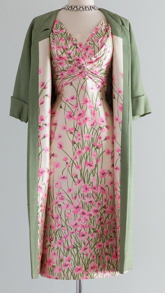 a vintage floral dress and a light green coat. the dress has a cream background with a pink floral pattern and a twisted bodice. the coat is light green with a simple design. a pearl necklace is visible at the neckline.