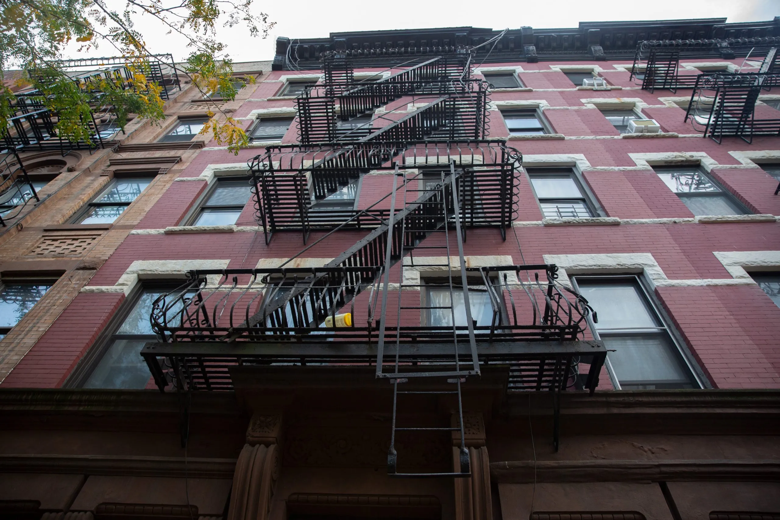 a lowangle shot of a classic red brick apartment building facade in new york city, featuring black fire escapes with intricate metalwork. the perspective emphasizes the height and verticality of the building.  the warm, earthy tones of the brick and the contrasting black fire escapes create a visually striking image.