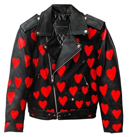 the image shows a black leather moto jacket adorned with a pattern of red hearts. the jacket has classic moto details like a belted waist, an asymmetrical zipper closure, shoulder epaulettes, silver studs, and a quilted lining visible at the collar. the red hearts are spread across the jacket's body and sleeves, creating a bold and eyecatching design.