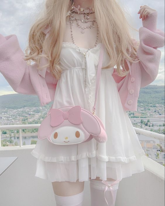 a woman with blonde hair stands on a balcony, wearing a white dress, pink cardigan, and thigh high socks. she has a pink my melody purse and several necklaces. the background shows a cityscape.