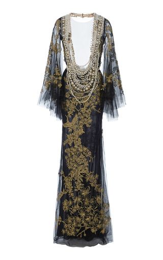 a long, embellished black gown with gold accents is shown against a white background. the gown has long, sheer sleeves and a long skirt that flares out at the bottom. the neckline is adorned with an elaborate necklace of beads. the gown is made of a sheer mesh fabric with gold embroidery.