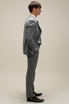 a man is wearing a grey suit and a tie. he is standing in a studio, looking to his right. he is looking very professional.
