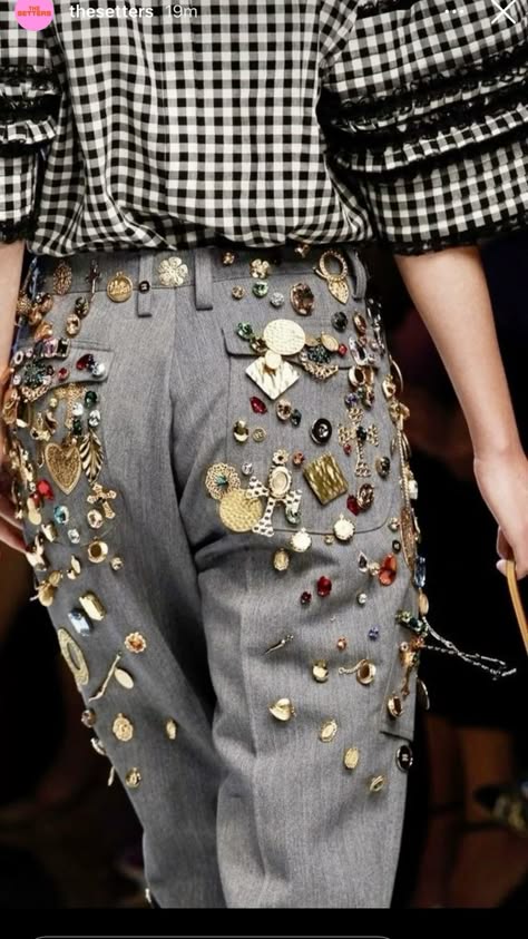 a closeup shot of a woman wearing a grey plaid shirt with a black and white gingham pattern, over grey pants covered in brooches. the model is showcasing the intricate designs of the outfit on the runway, and the photograph captures the fashion trends for the season. the image highlights the unique and stylish appeal of the outfit, showcasing the attention to detail and the overall aesthetic of the clothing.
