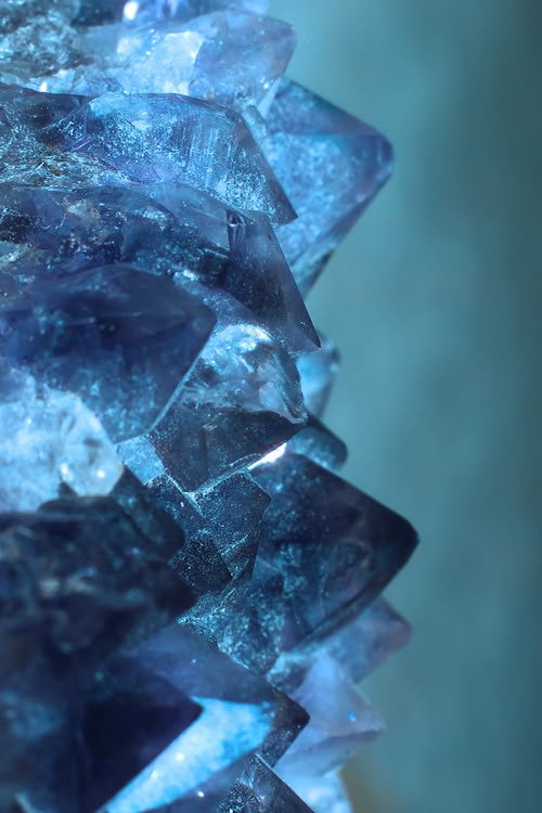 a closeup of a blue crystal mineral, showing its textured surface and geometric shapes. the crystal appears dark and shiny, reflecting light.