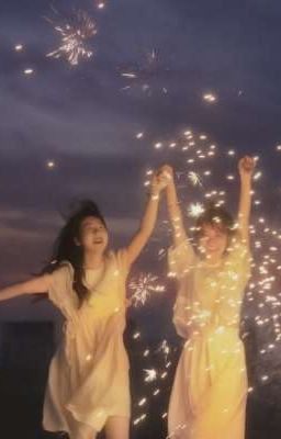 two women in light yellow dresses are holding hands and jumping in the air. they are surrounded by fireworks. the background is a dark blue sky.