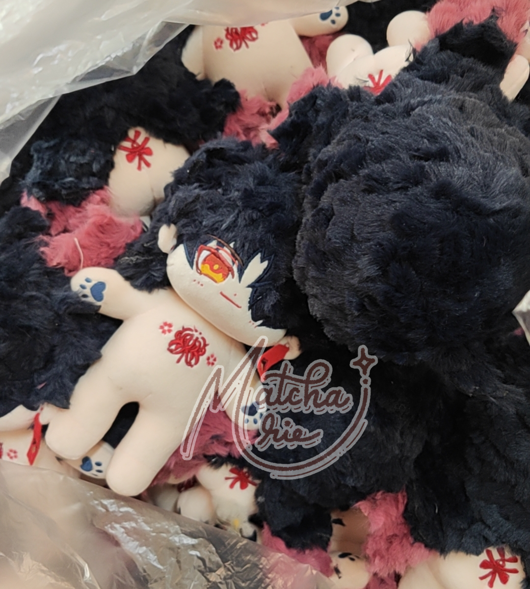 a closeup shot of a black and white animeinspired plush toy surrounded by other plushies in a bag. the plush toy has long black hair, red eyes, and a white body. the other plushies are mostly pink and white. the photo was taken in a slightly blurry manner. the background is a clear plastic bag.