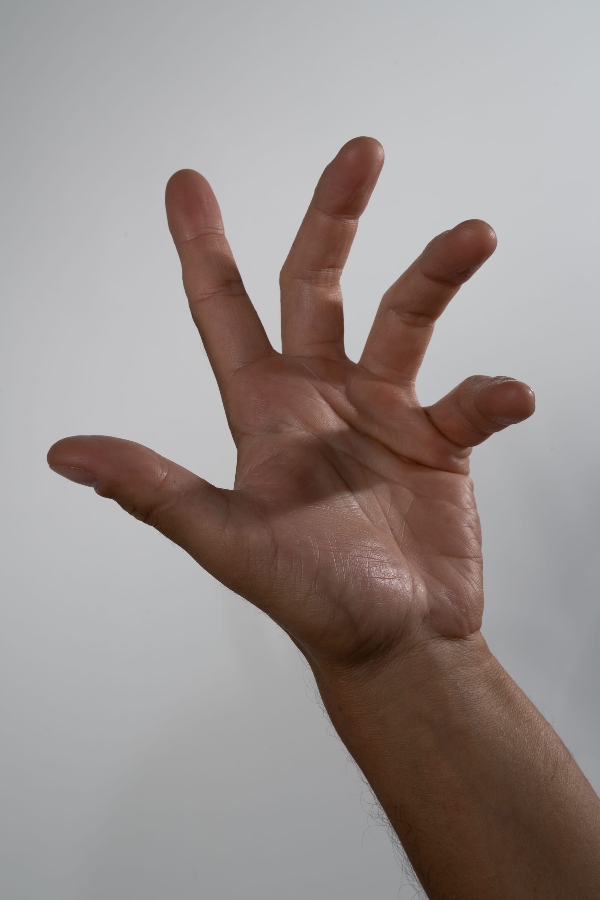a closeup image of a person's hand, extended towards the viewer. the hand is positioned with fingers splayed, showcasing the palm and details of skin texture. the background is a neutral, bright white, emphasizing the subject.