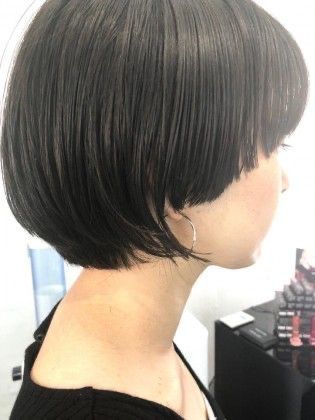 a woman with short black hair is posing for a headshot. she is looking to the right of the frame, and her hair is styled in a bob with the ends slightly curled inward. she is wearing a silver earring and is looking to the right of the frame. her skin is fair and flawless, with a subtle glow.